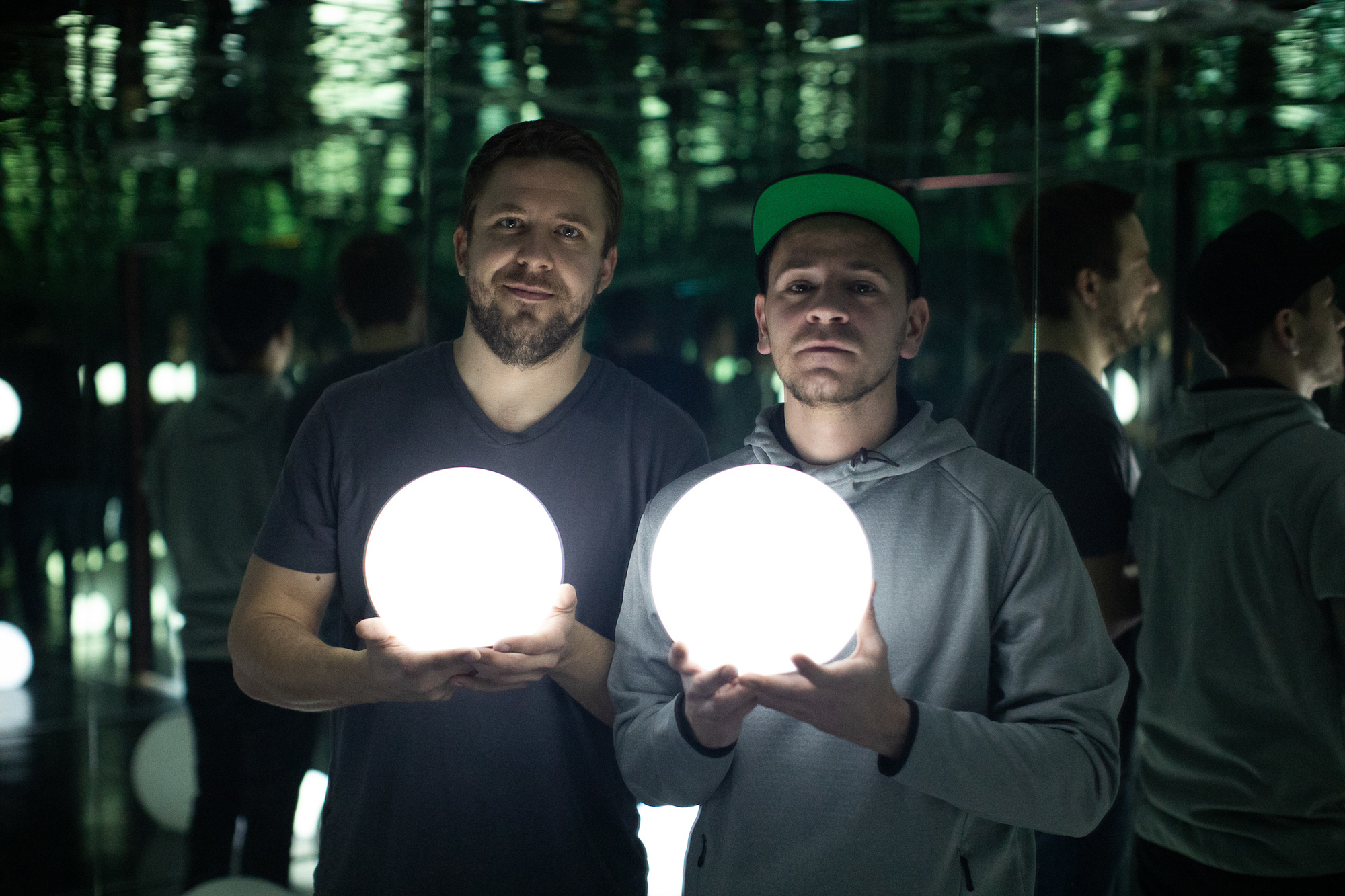 Two men standing in a mirror-clad room carrying glowing sphere lamps.