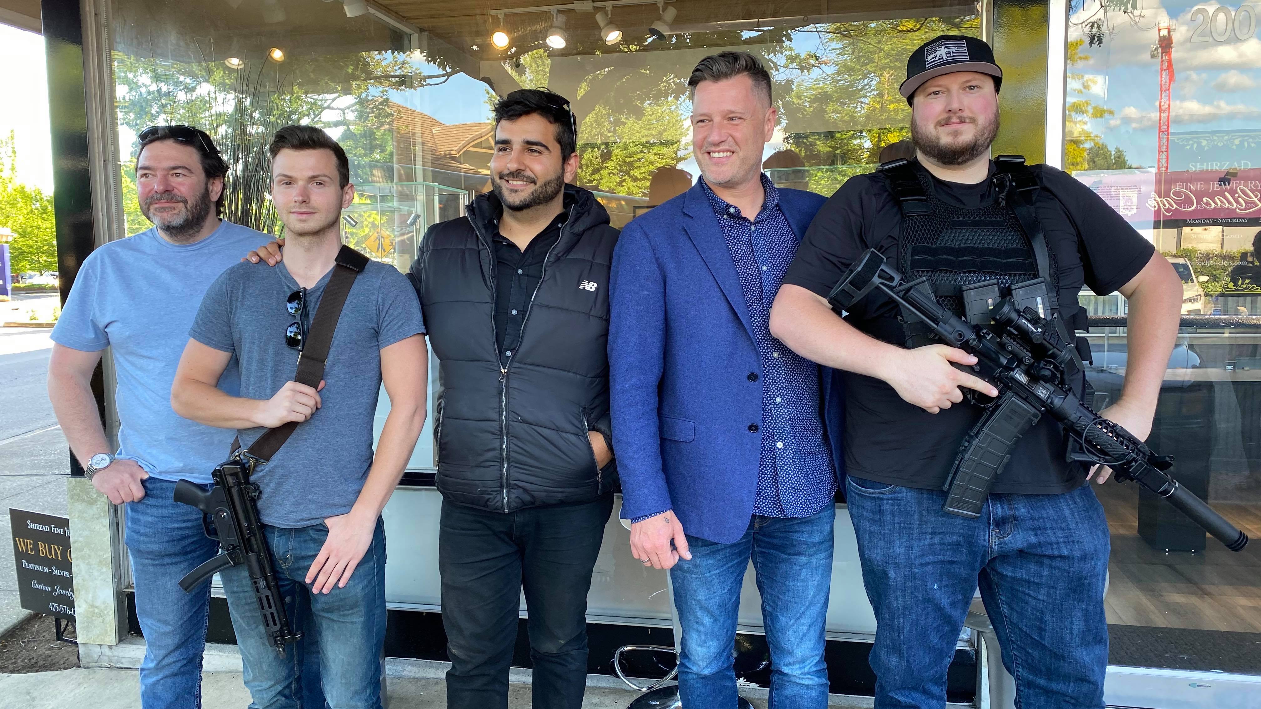 Five men stand together in front of a business, two with AR-15s