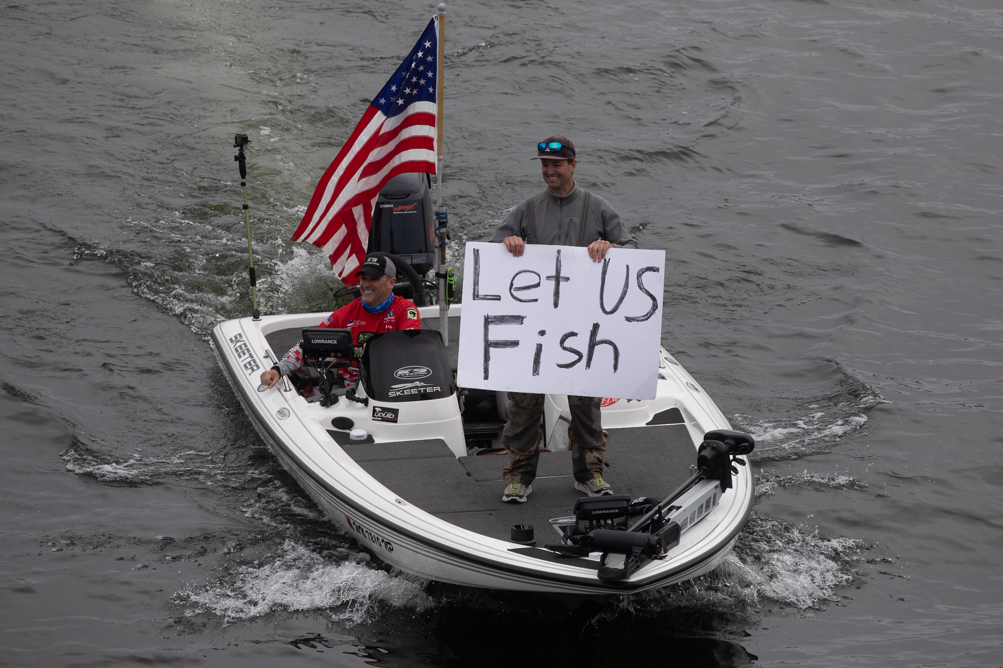 A man stands up in a boat in the water with a sign that says let us fish