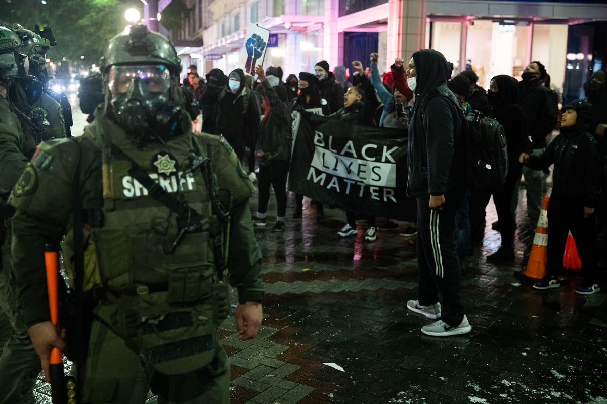 officers in riot gear stand near BLM protesters