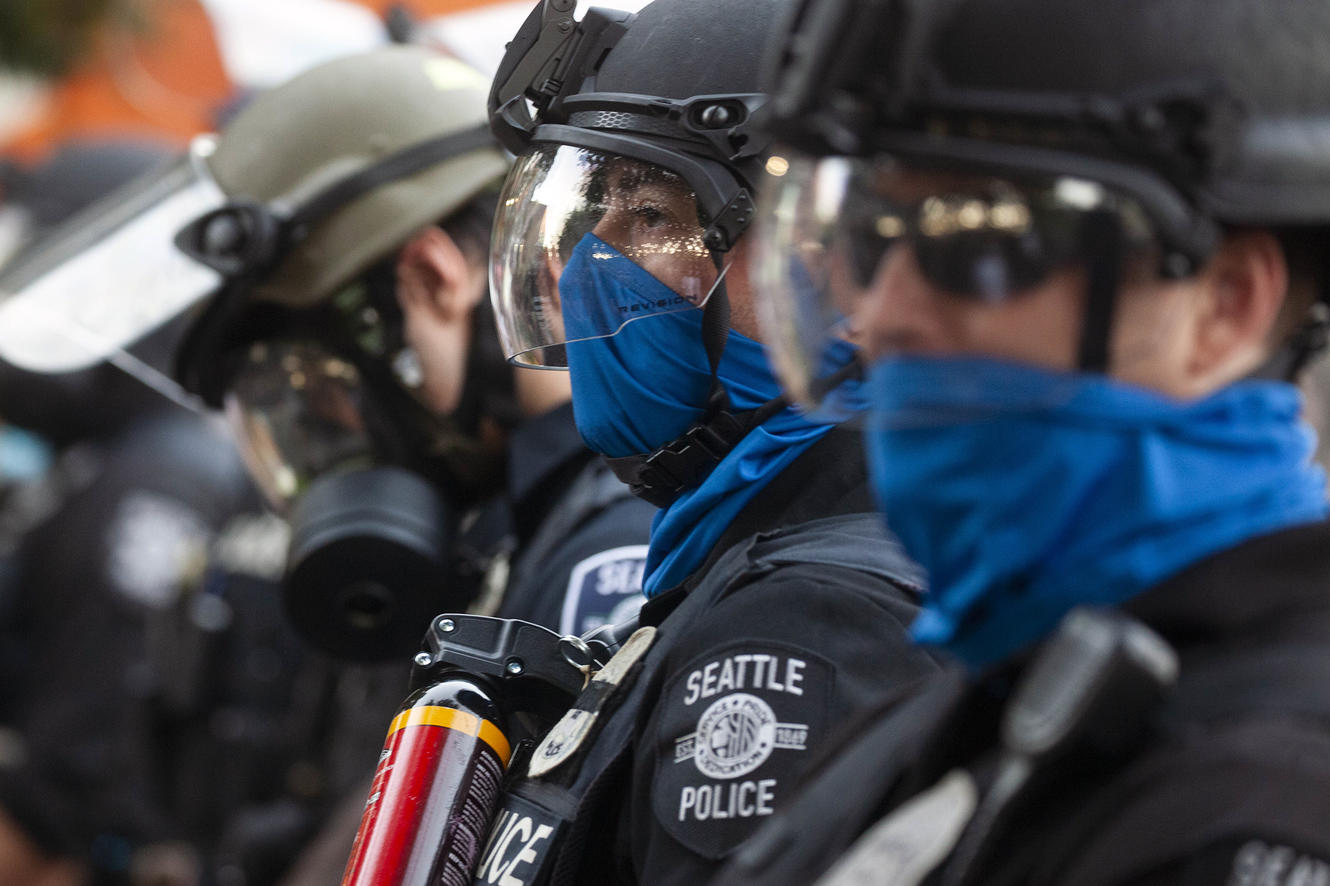 A line of SPD officers wearing helmets, face shields, and gas masks