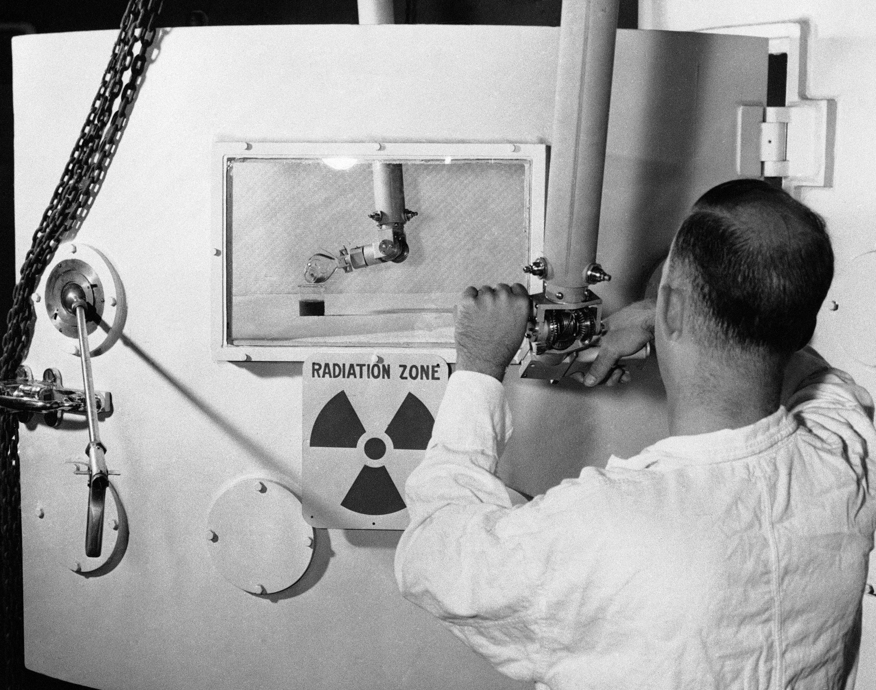 A man works a lever in front of a sign that reads “Radiation Zone”