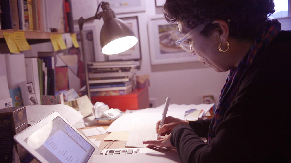 Claudia Castro Luna writing at a desk
