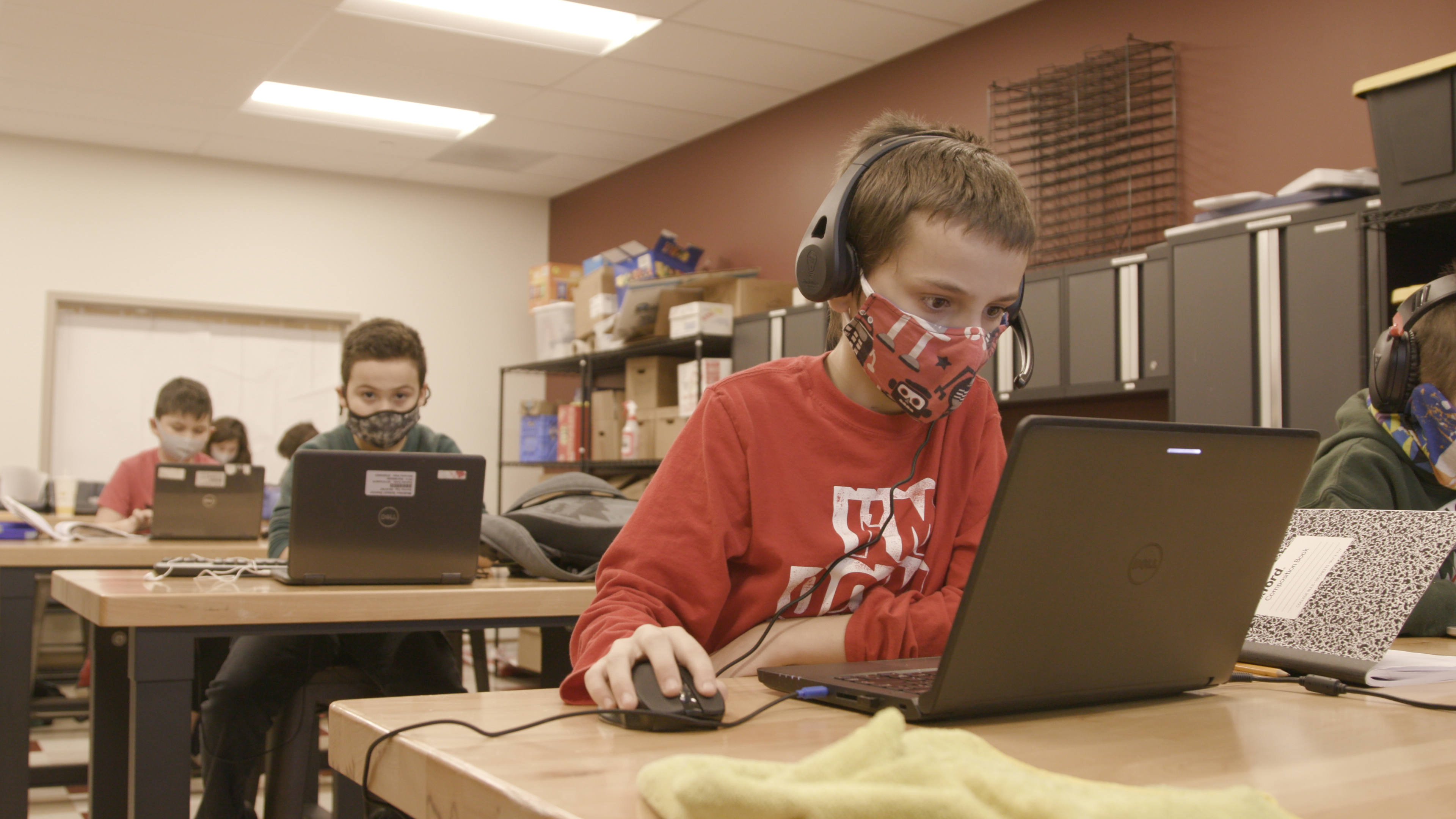 Children work at laptops while wearing masks