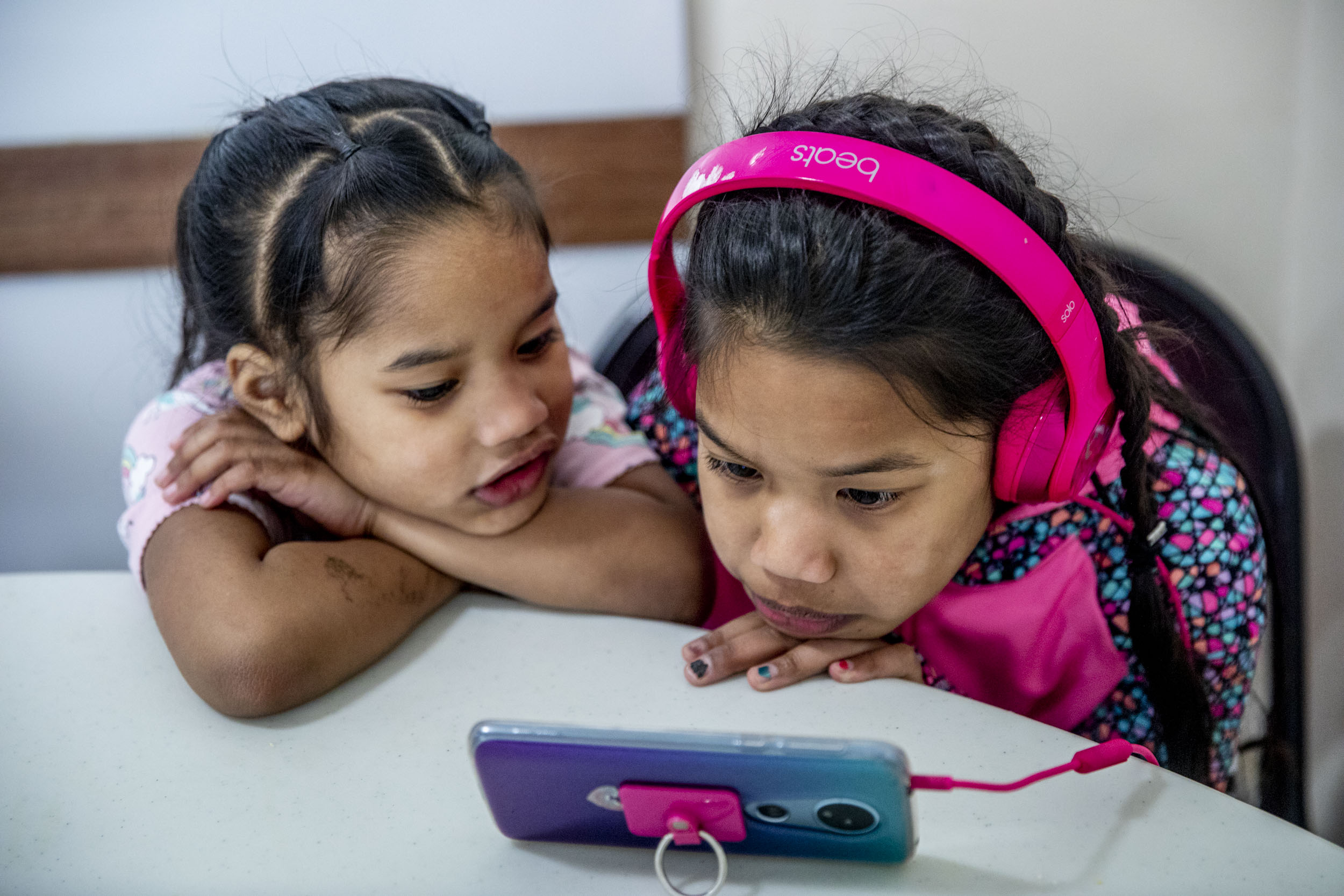 Sisters Faith, 4, left, and Zinnia Lejer, 7, watch cartoons on a phone in the common area at Mary's Place homeless shelter in Burien on March 1, 2019. (Photo by Dorothy Edwards/Crosscut)