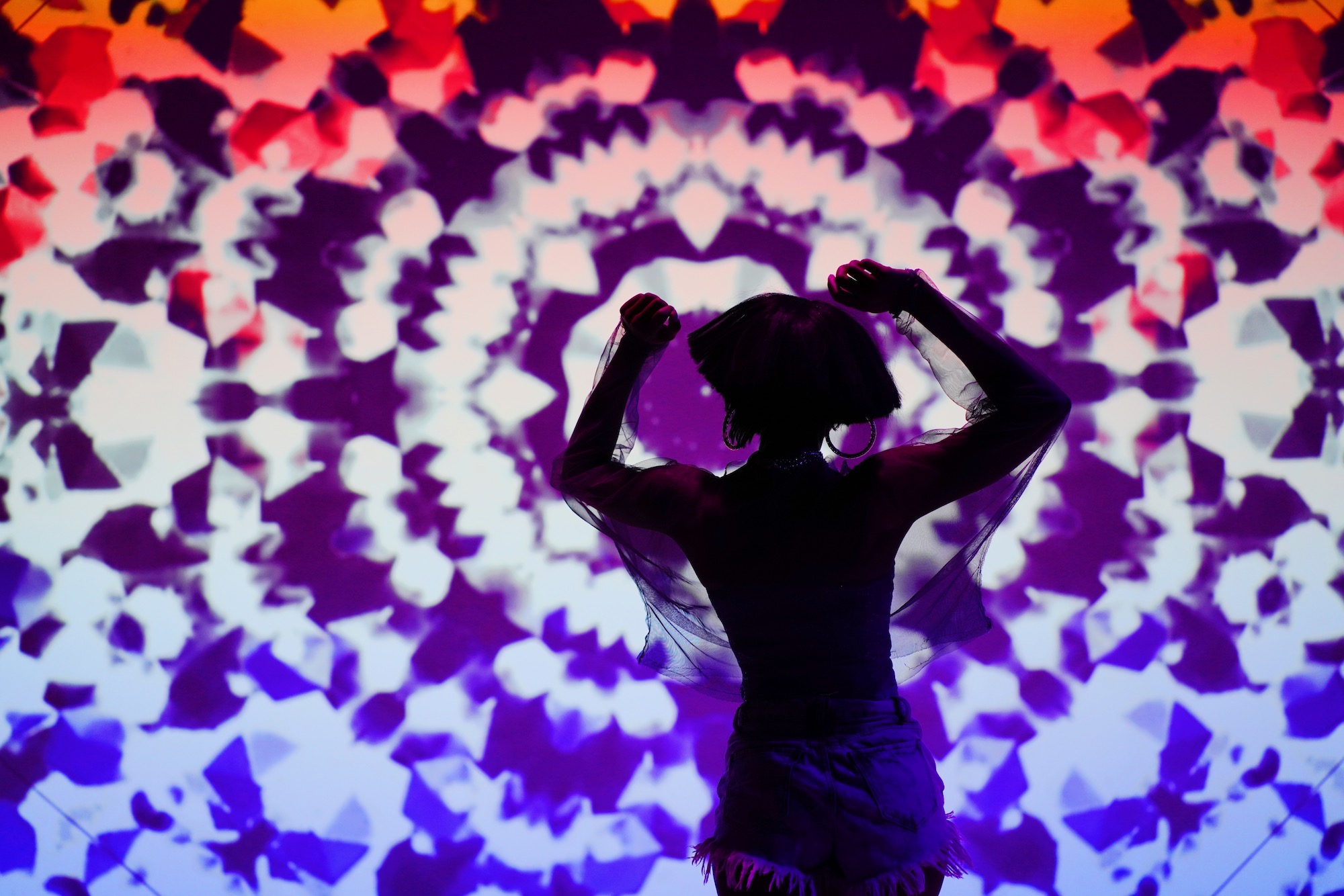 a woman dancing in front of a wild tie-dye screen