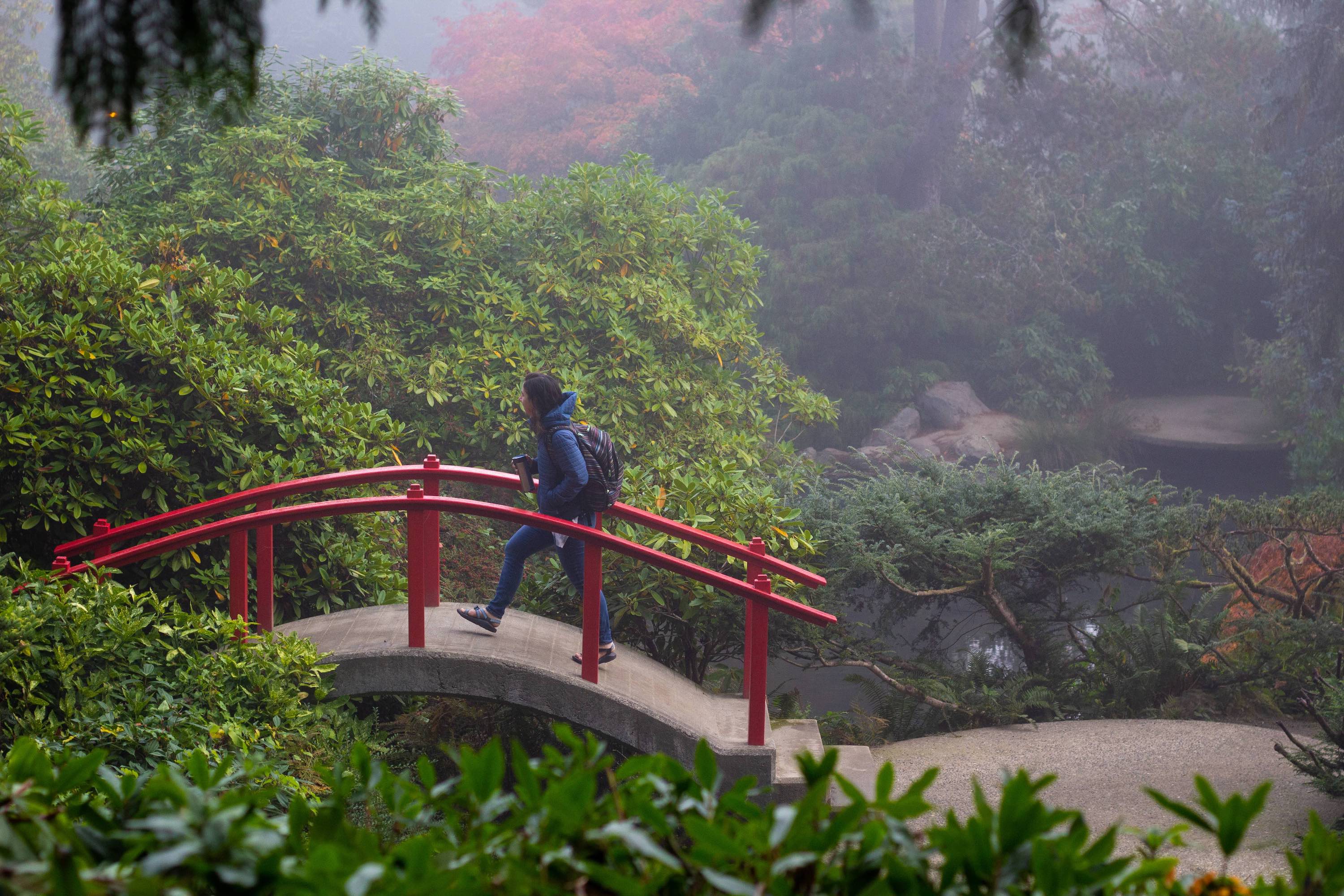 a woman crossing a red bridge in a park