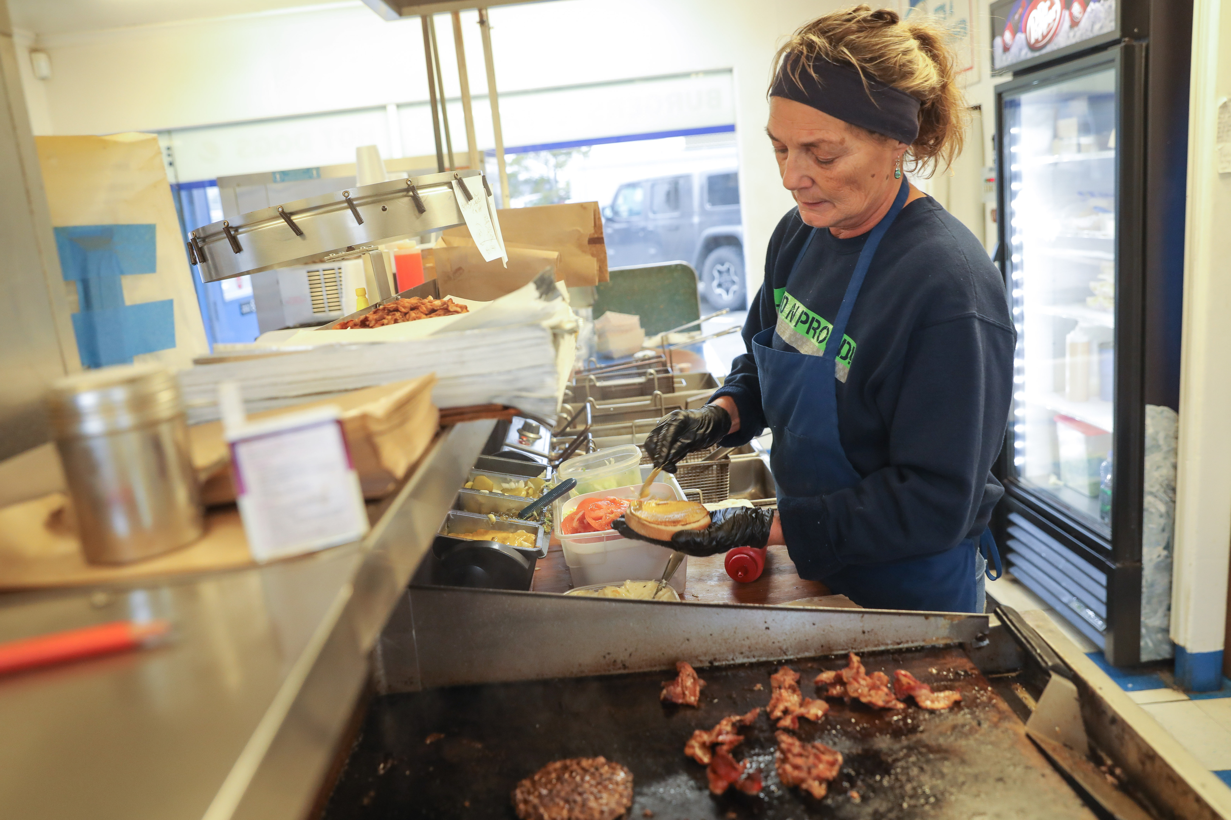 A woman wearing blue cooks burgers at a restaurant kitchen stove
