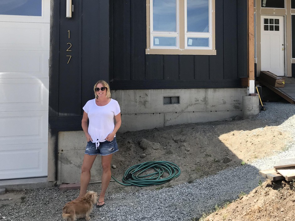 A blonde woman, former Pateros mayor Libby Harrison, stands in front of her home, which is still under construction.