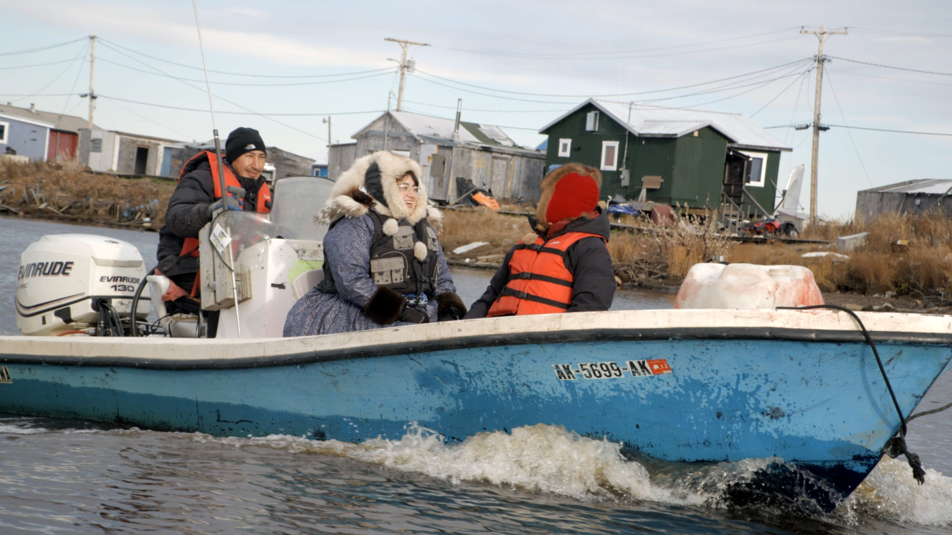 Three people in a small motorboat dressed in parkas and life-vests