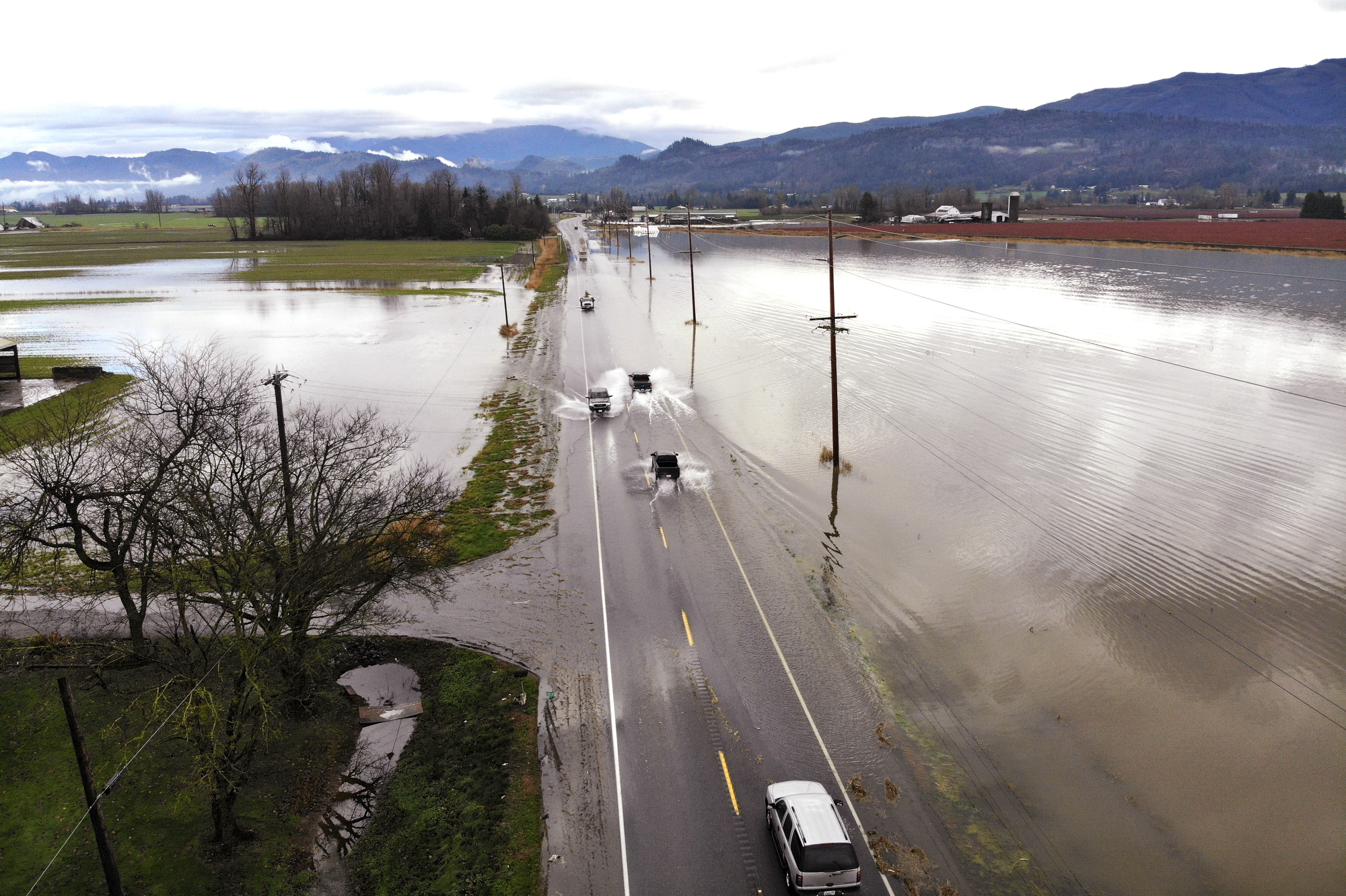 Cars driving over a partially flooded road going through flooded fields