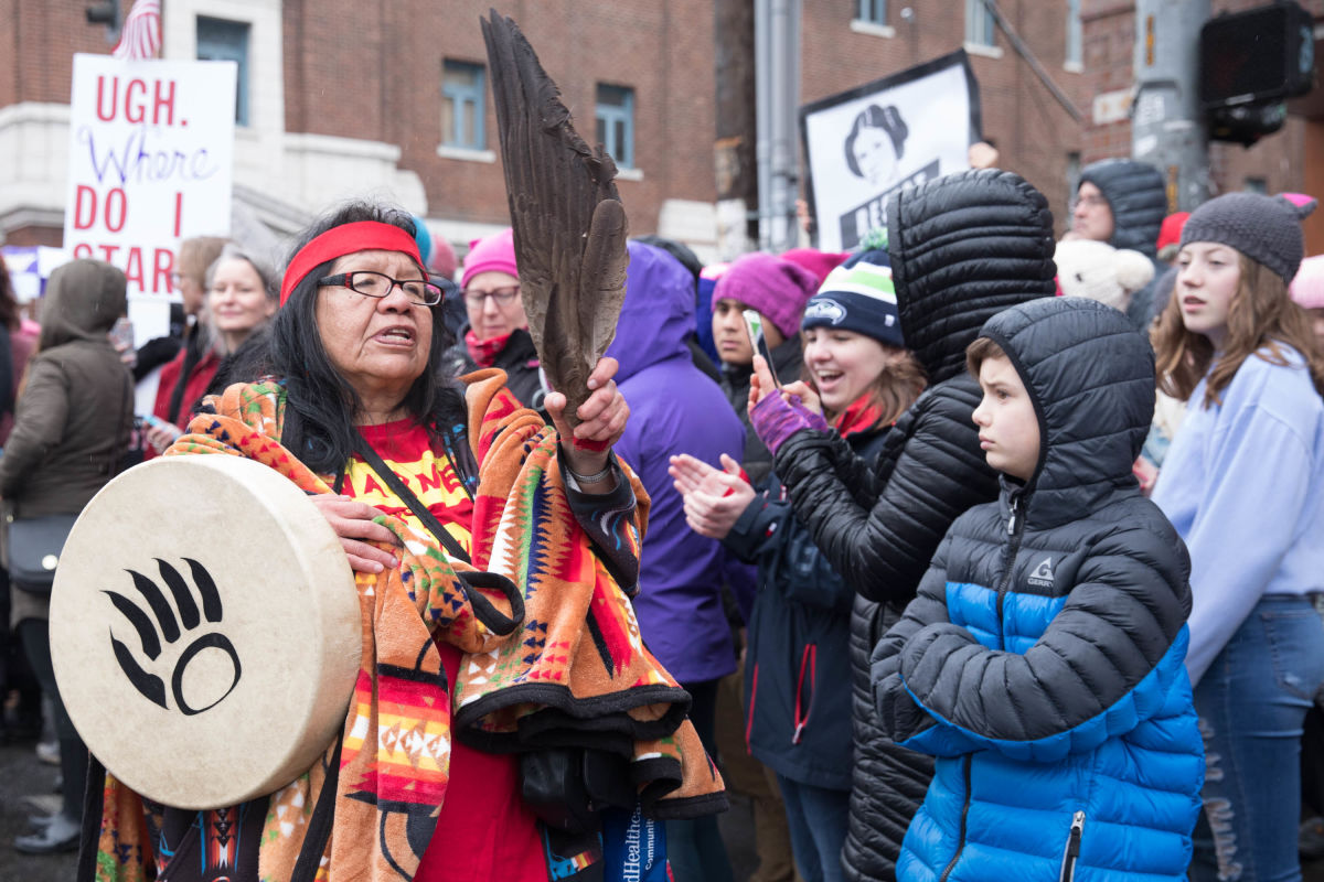 Holding a cluster of bird feathers and a drum imprinted with a bear claw, Feanette Black Bear, of the Lakota Nation, walks with the group, Murdered and Missing Indigenous Women, which led the Seattle Women’s March 2.0 in Seattle, Jan. 20, 2018.