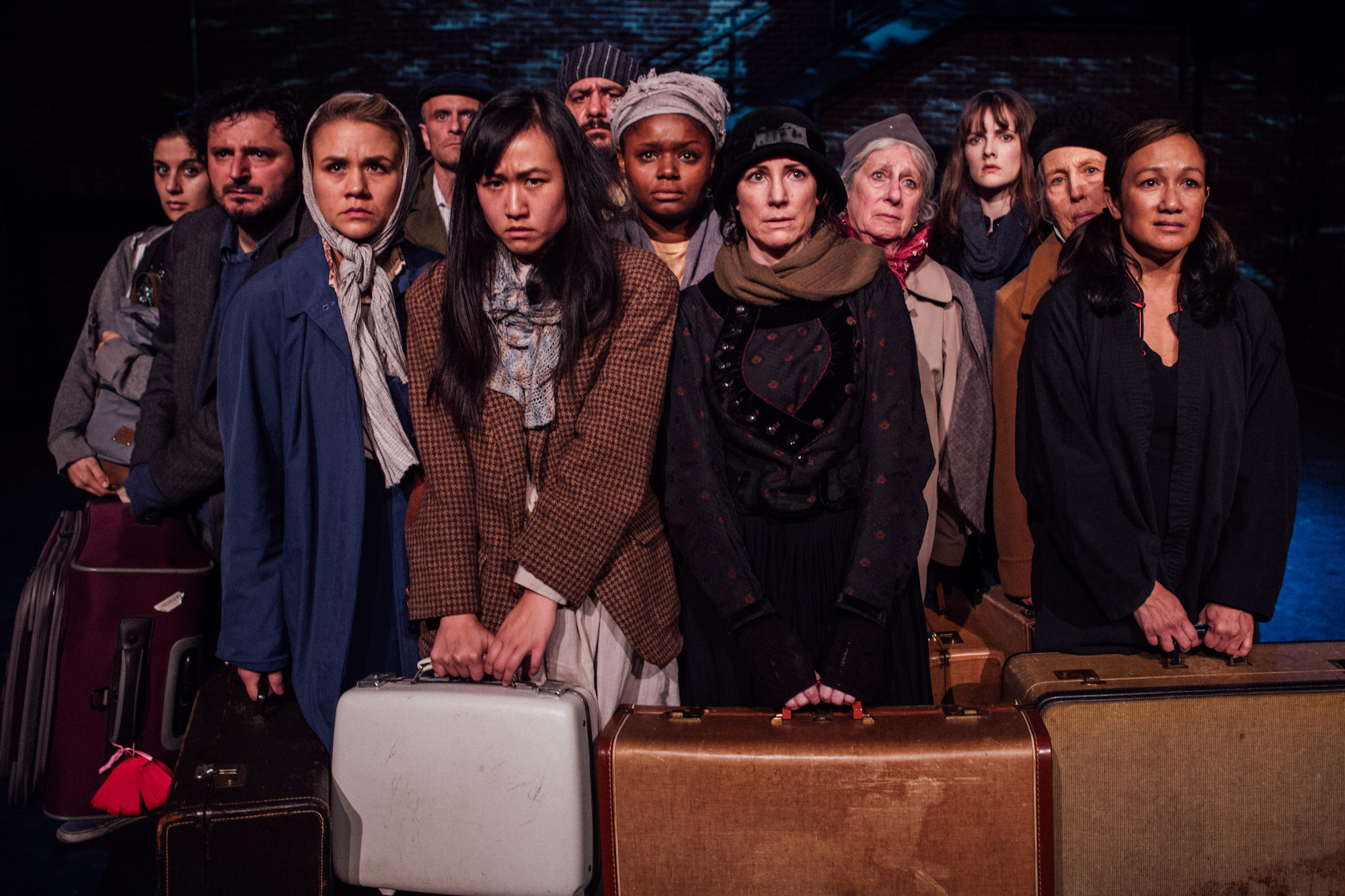 a group of people on stage dressed as immigrants with suitcases