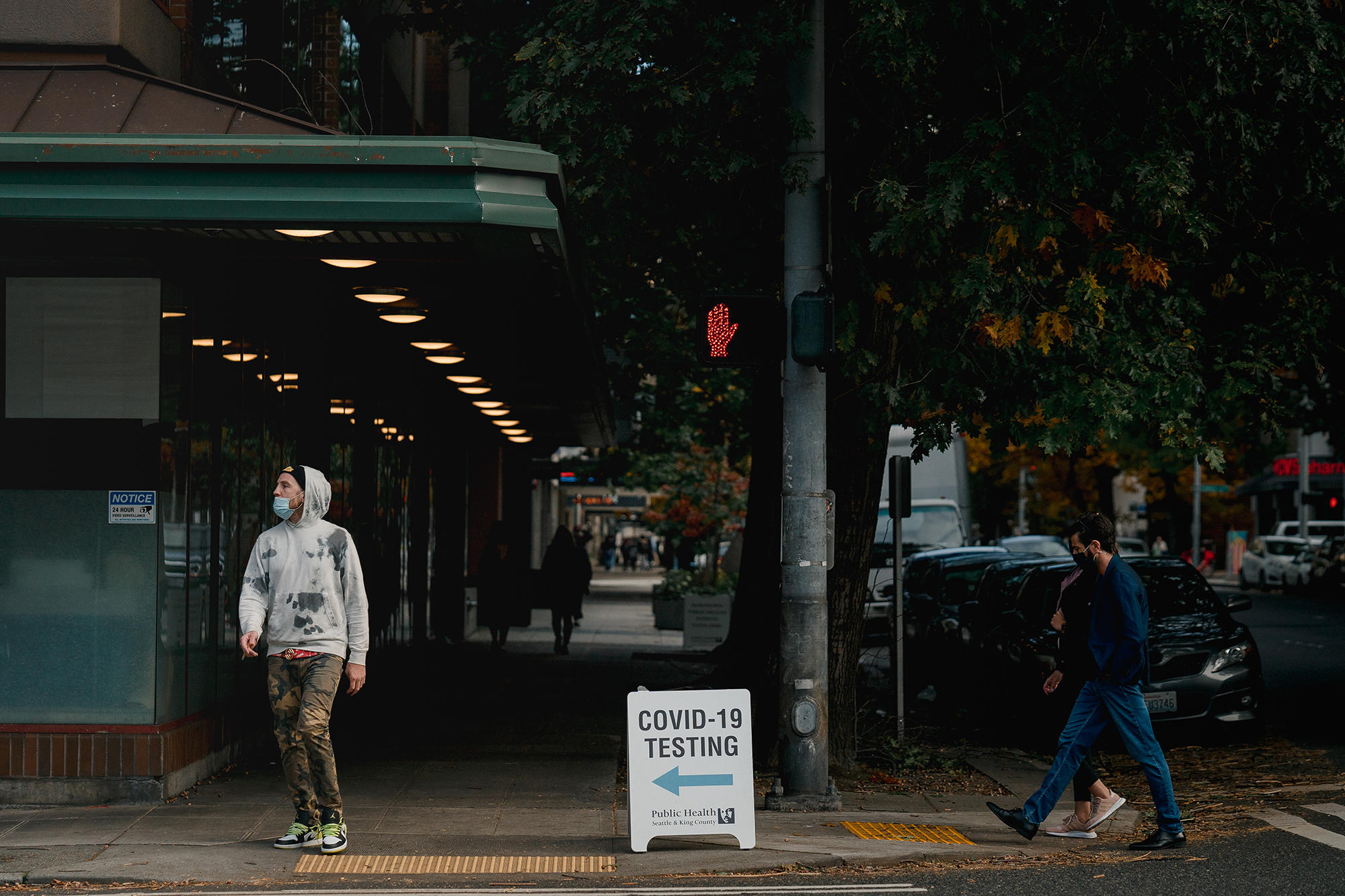People wearing masks walk by a sign offering COVID-19 testing.