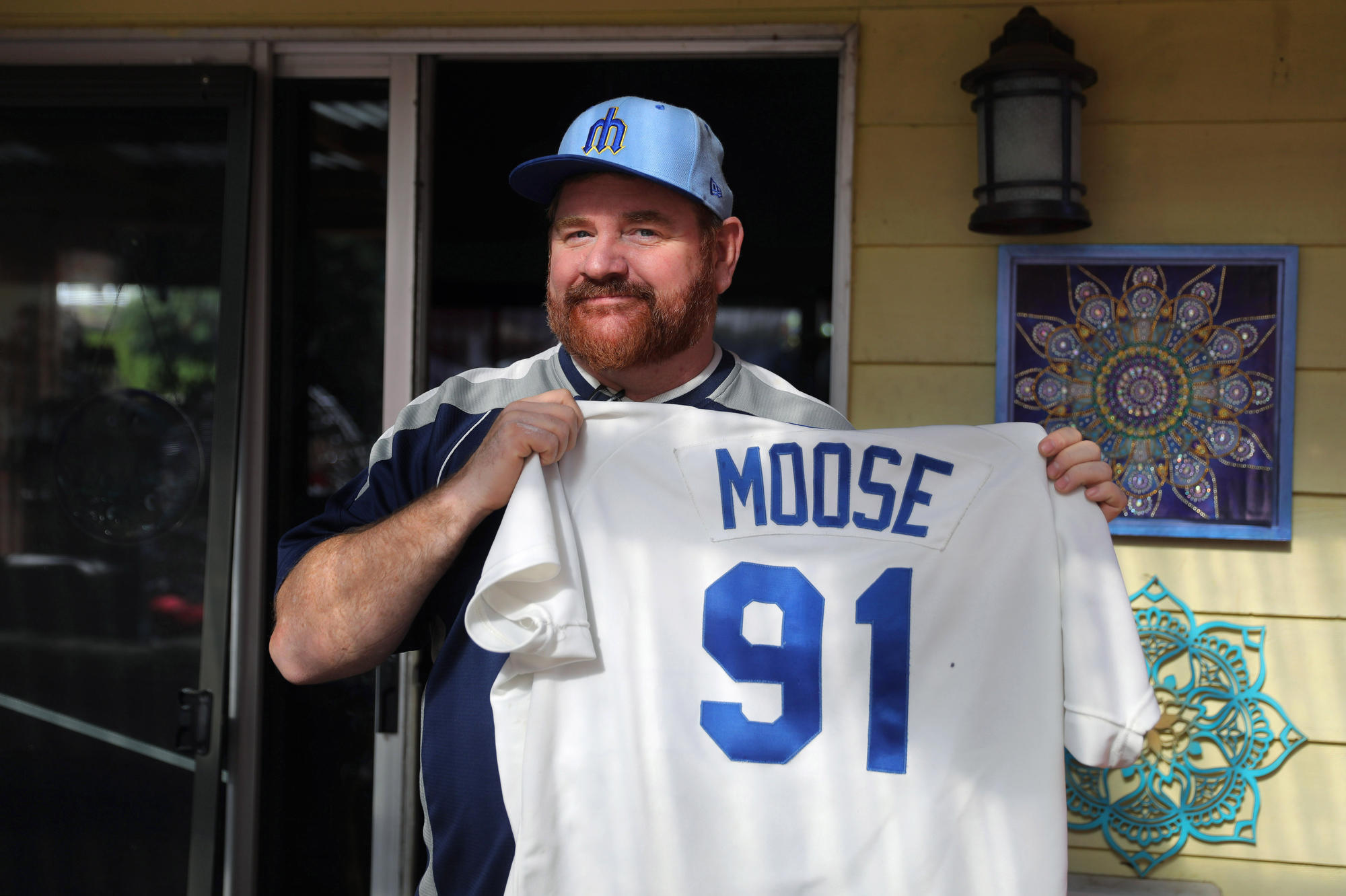 A man holds up a white baseball jersey with Moose 91 on the back