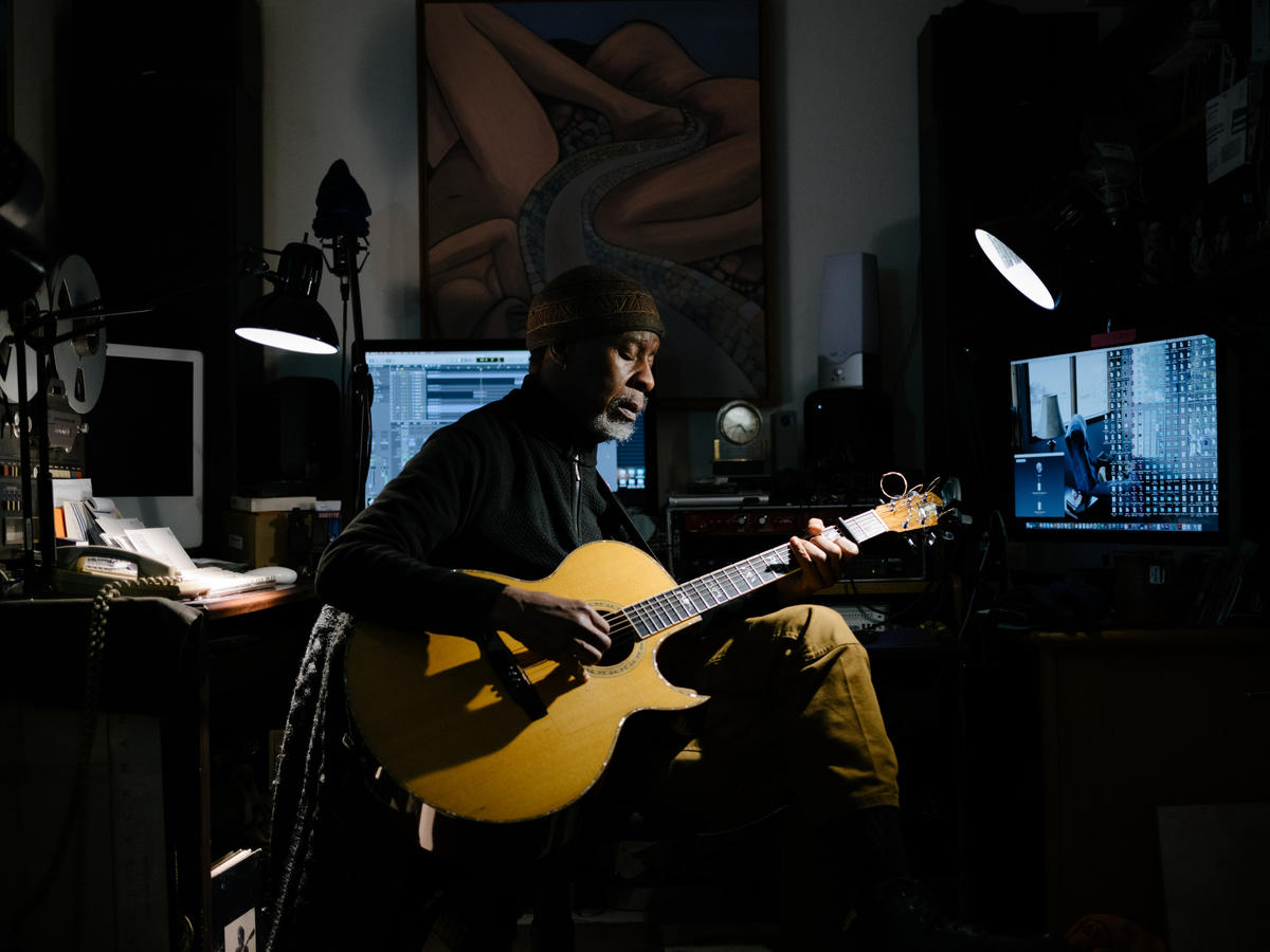 Person in studio with guitar lit by a light and blue screens behind