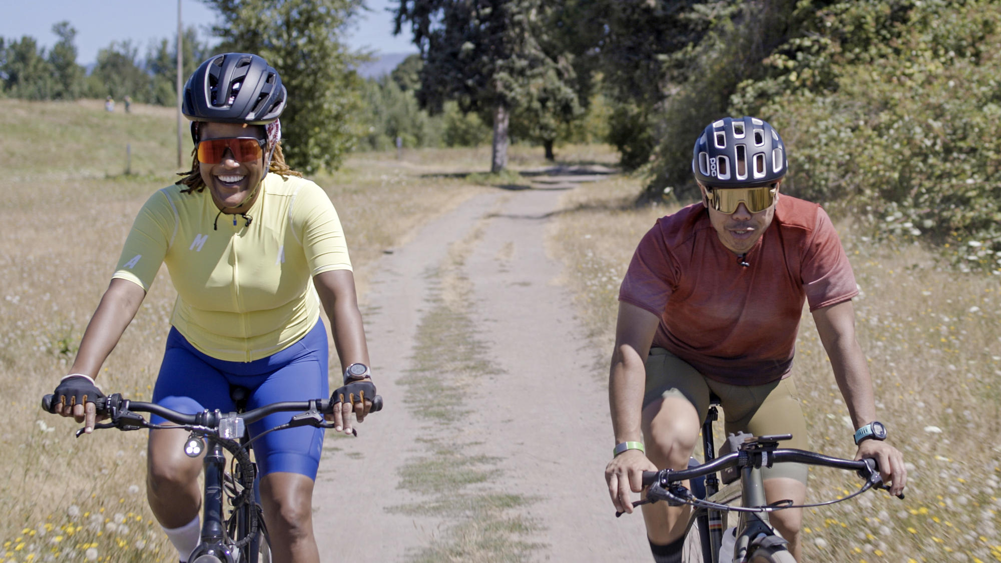 bipoc woman and man riding a bicycle on a gravel path