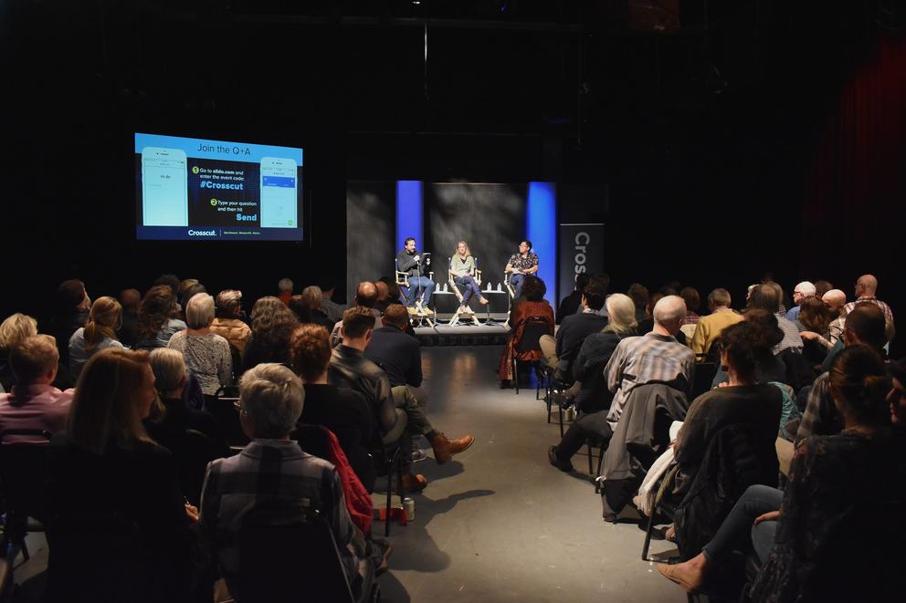 Three panelists discuss climate change before an audience in a darkened studio