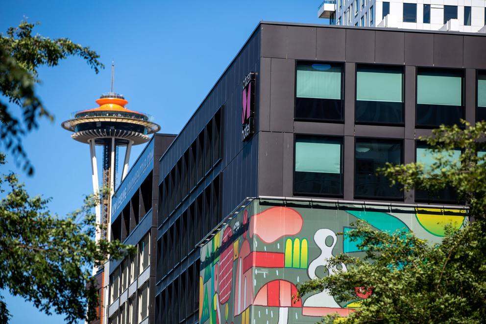 an orange-topped space needle peeks from behind a hotel building
