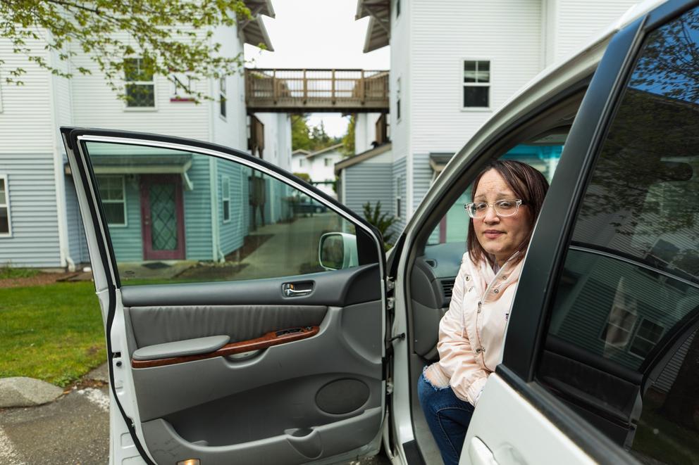 A woman wearing glasses sits in her car with the door open