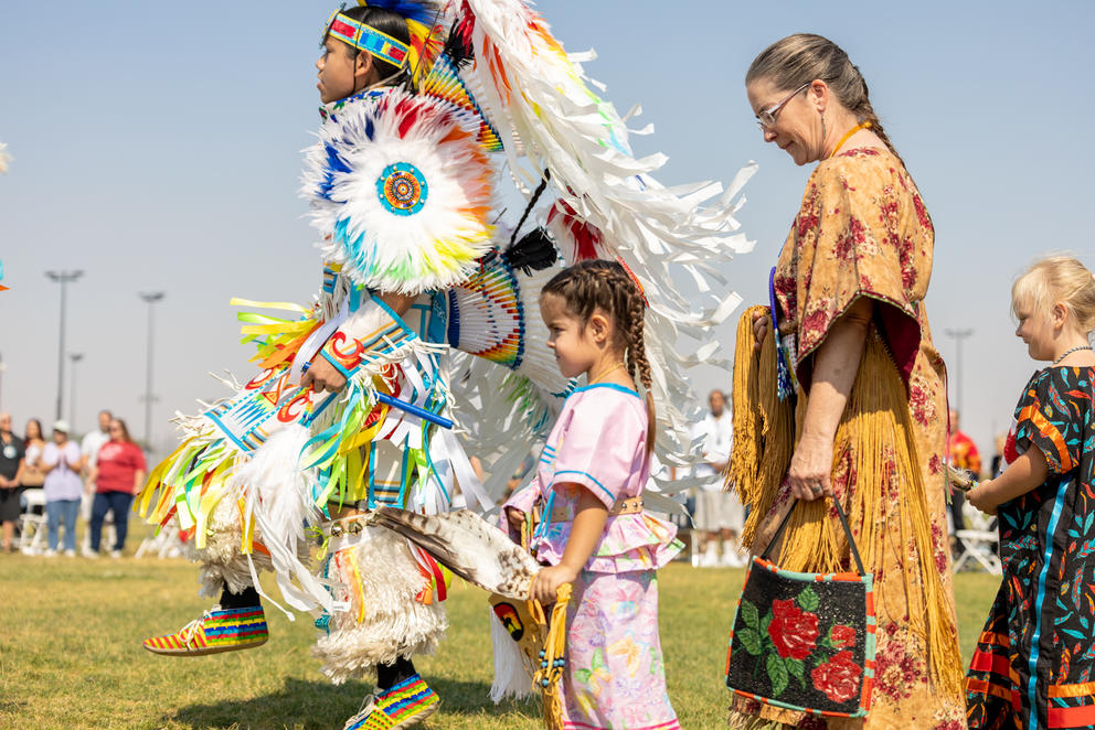 Four powwow participants, two of whom are children, in regalia