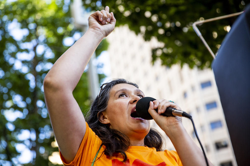 A woman speaks into a microphone with her fist raised in the air