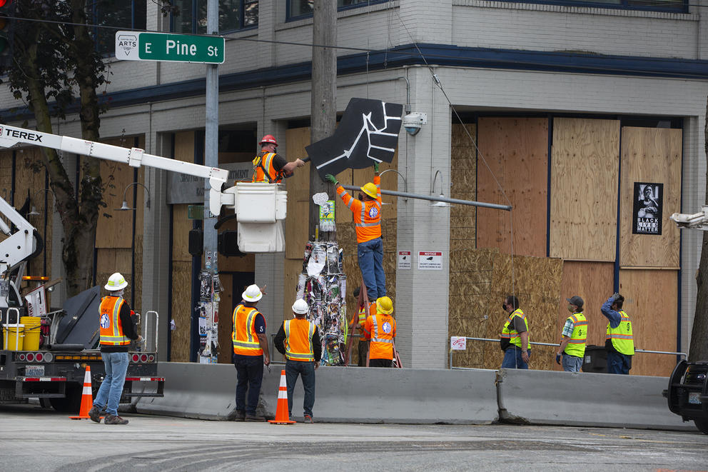 People in orange vests dismantling an artwork from a light pole