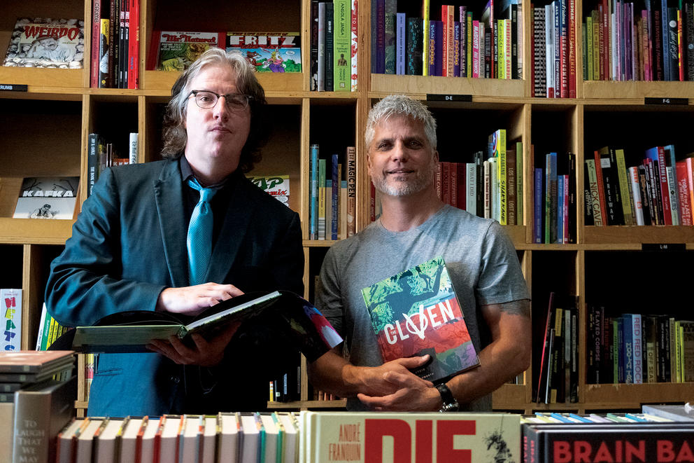 An author and artist stand for a picture in front of bookshelves