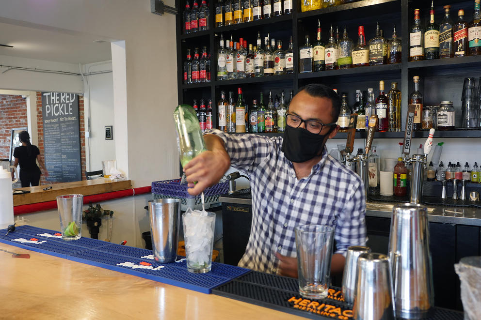 A man at a bar pours an alcoholic beverage with a mask over his face