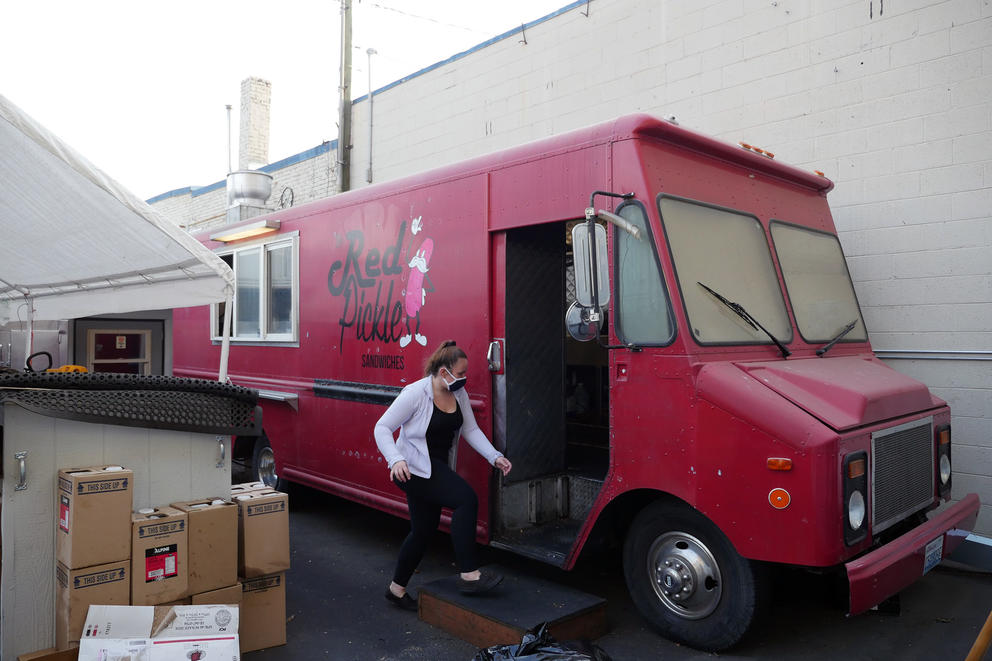 A woman with a face mask walks into a bright red foot truck parked outside