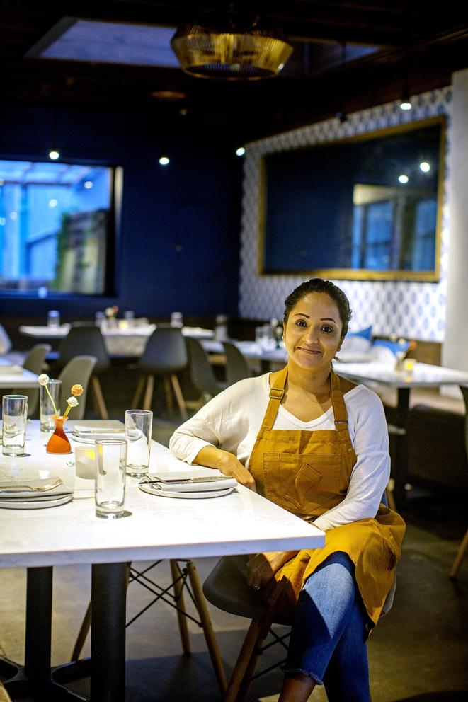 woman with apron sitting at table in empty restaurant, smiling at camera 