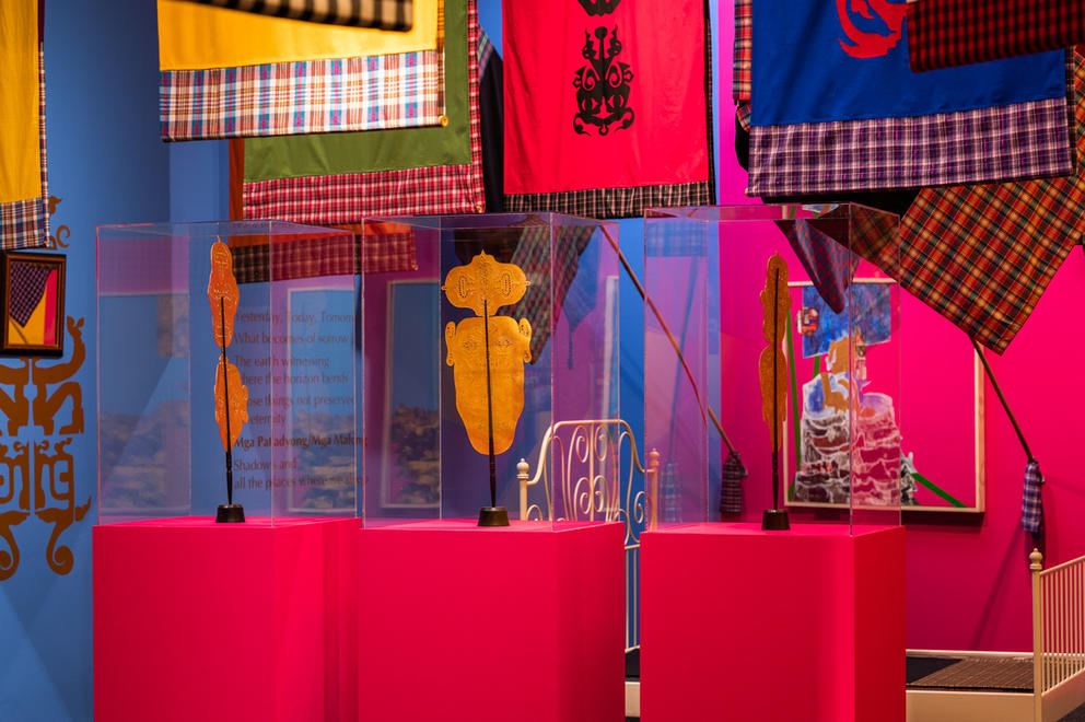 Flags in various colors, bright pink pedestals with golden masks and blue walls int he background
