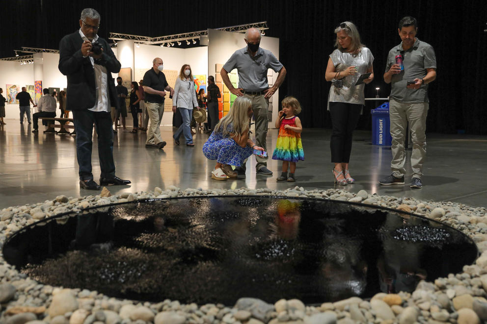 People stand around a pool of dark liquid, surrounded by gray stones