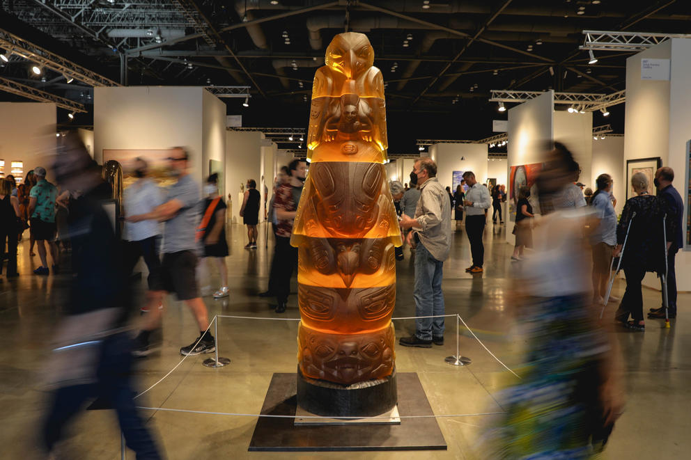 An amber totem pole featuring Tlingit imagery while people walk near it