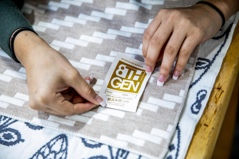 Hands on a beige and white blanket adding a golden "Eighth Generation" label to the blanket
