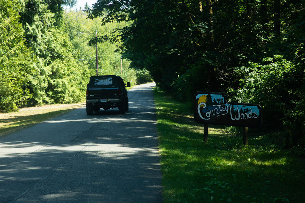 A car drives along a road surrounded by trees and a sign that says "Country Woods"