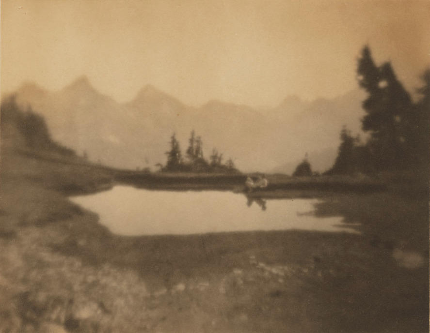Sepia-toned image of mountain scene with alpine lake and trees, man reclining naked near lake