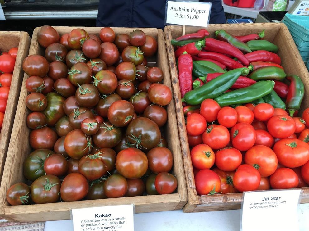 At left, tomatoes are displayed with deep red and green tones. At right, bright red tomatoes and peppers are mingled in a display box