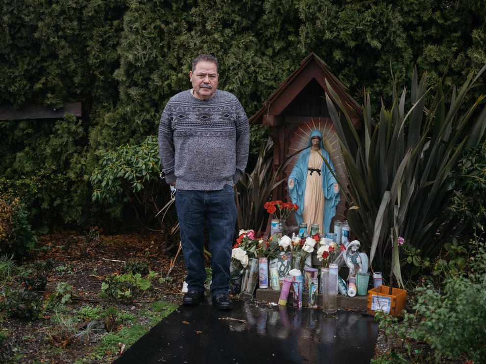Jose Ortiz stands near a statue of Virgin Mary surrounded by prayer candles