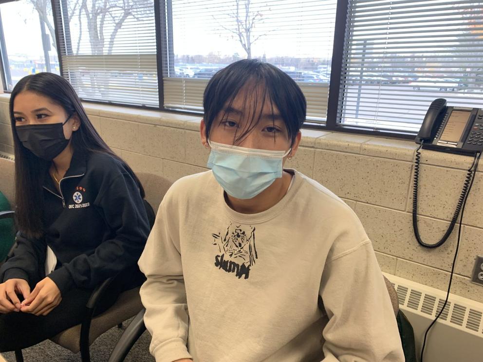 Kenji Lee sits next to another student in a classroom. Both wear face masks