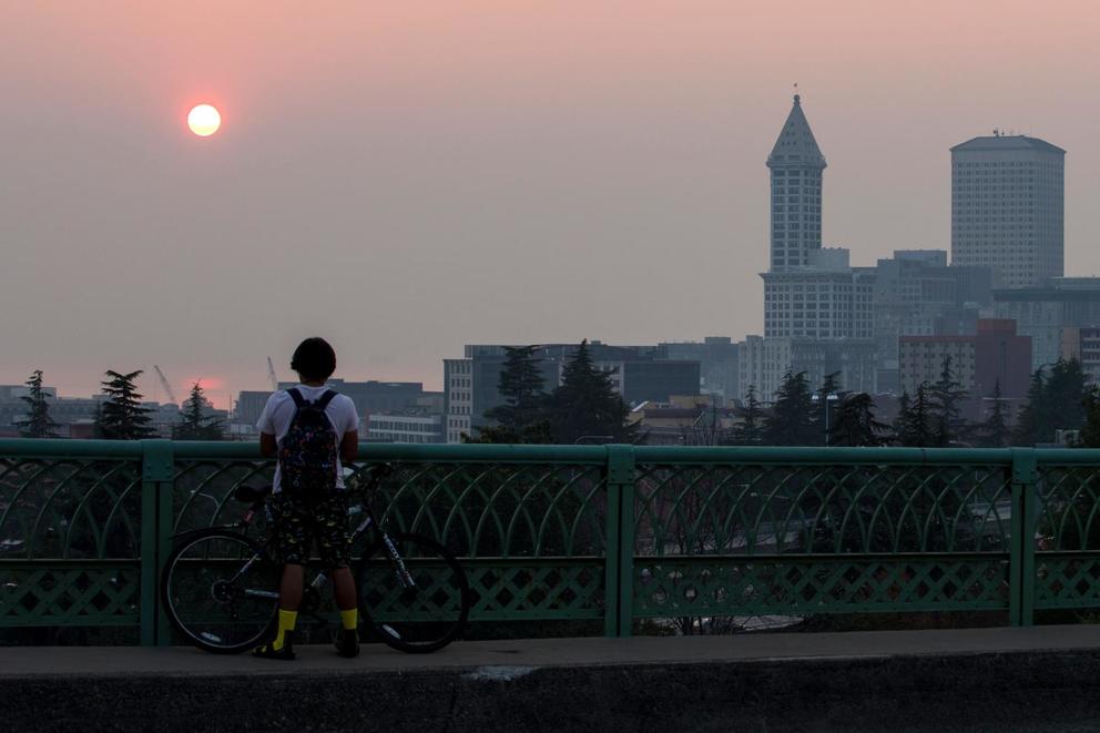 A man stands on the Jose Rizal Bridge in Seattle and looks out at a smoky sunset caused by wildfires in British Columbia