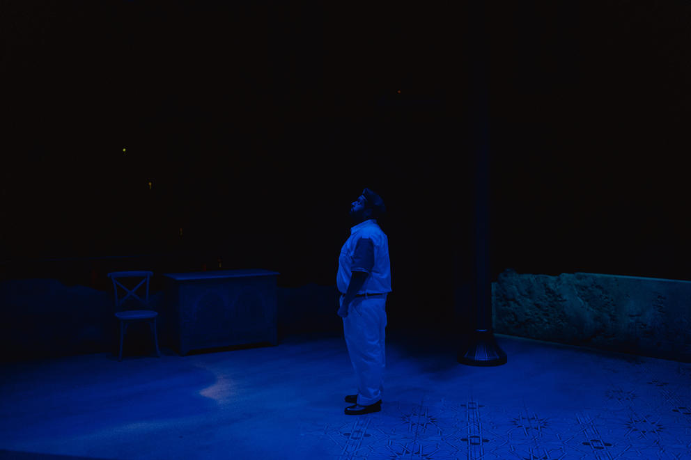 a dark scene on a theater stage where a man is looking up at the sky
