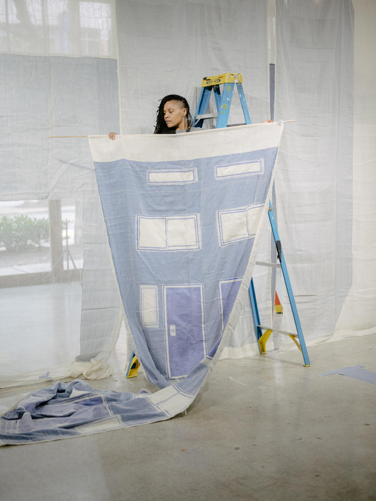 Person holding up a sheet with blue and white squares, standing on a ladder behind