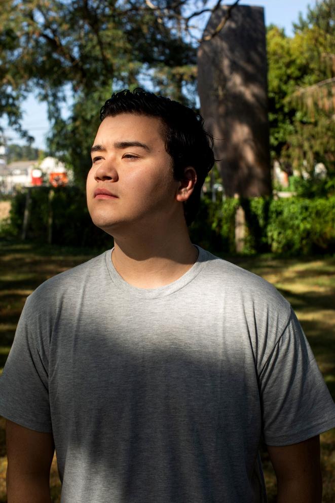 Andrew Hong looks off camera, with trees behind him and a shadow across his chest