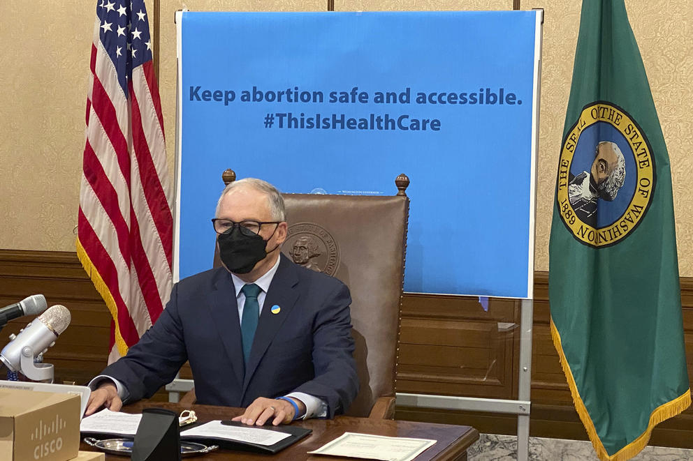 Jay Inslee sits while wearing a face masksa