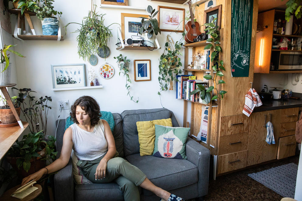 A woman sitting on a couch surrounded by wall-mounted plants and art