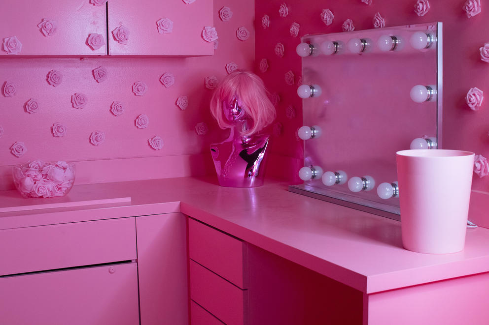 A pink bathroom counter, vanity mirror and pink wig in a pink-painted room.
