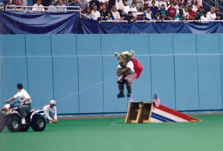 A moose on rollerblades is pulled over a jump by an ATV on a baseball field