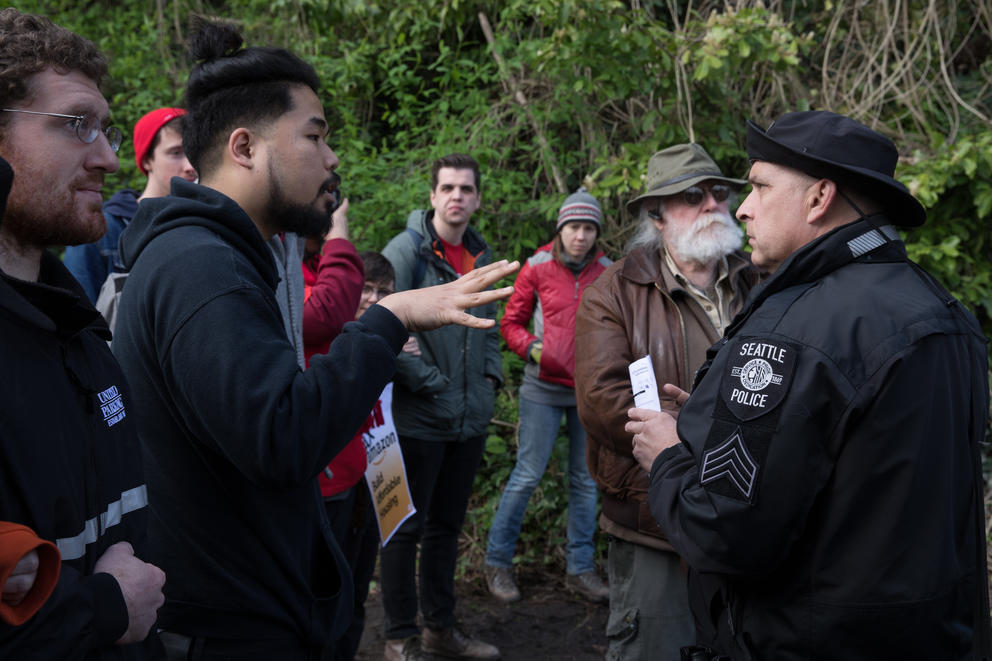 (From left) Activist Dae Shik Kim Hawkins Jr. speaks with Sgt. Zerr of SPD's Navigation team during a sweep of  Ravenna Woods homeless encampment near Seattle's University Village neighborhood, Tuesday, April 17.
