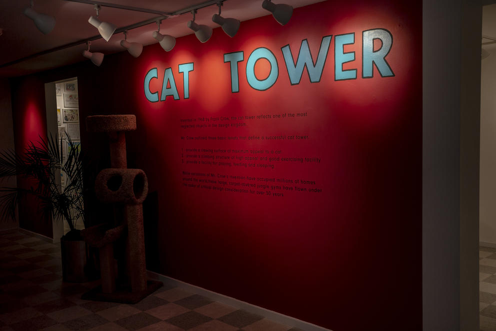 A red wall with CAT TOWER printed on it in blue text above a description of the exhibit